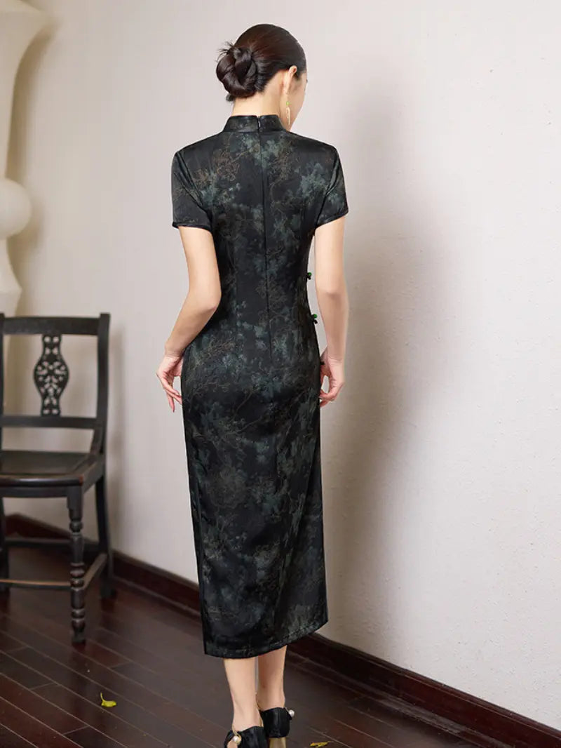 Woman wearing a Black & Deep Emeral Jacquard Satin Long Qipao With Green Buttons  standing against a white wall.
