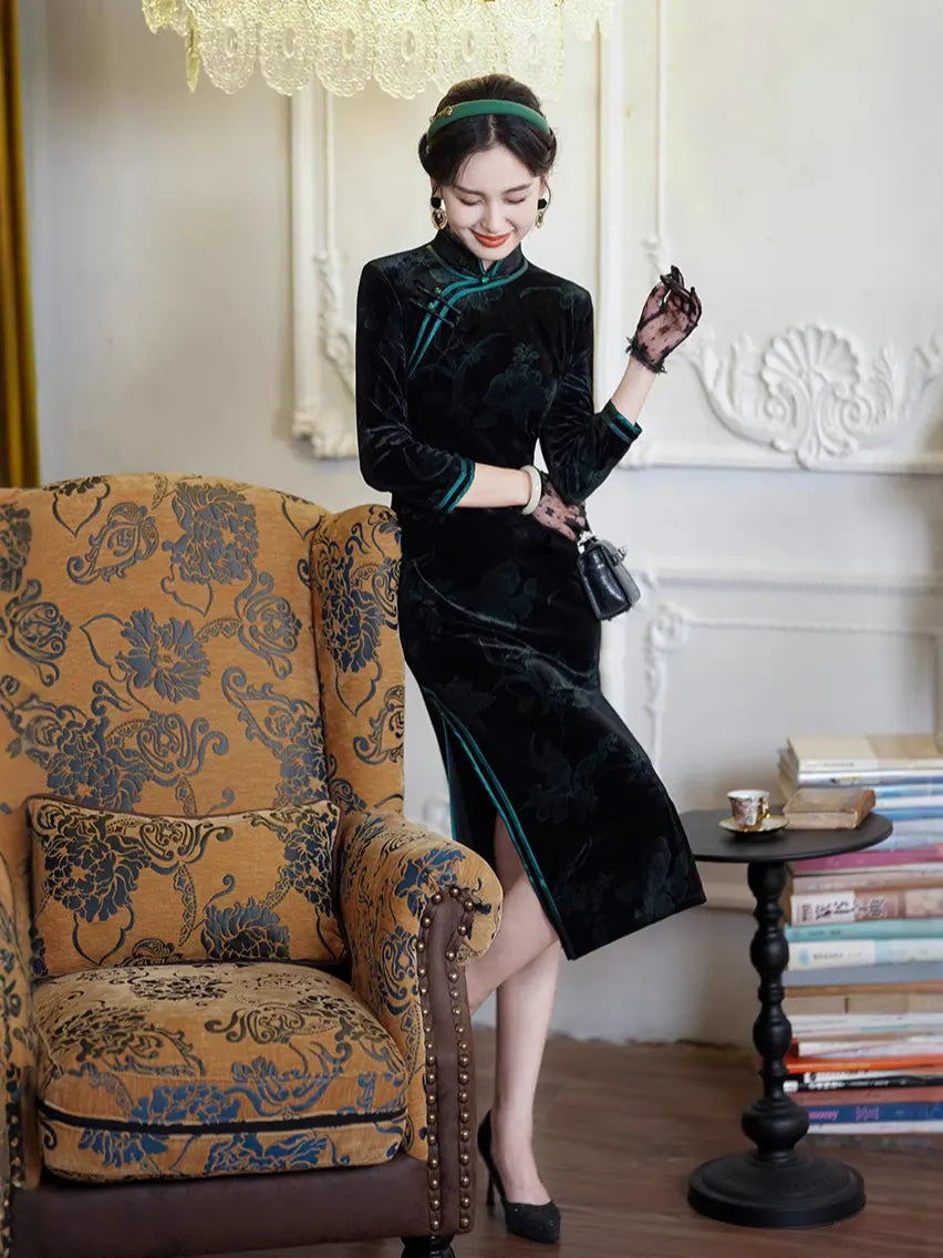 Woman in a Black & Emerald Green Velvet Long Sleeves Qi pao Dress standing next to an ornate armchair in a stylish room.