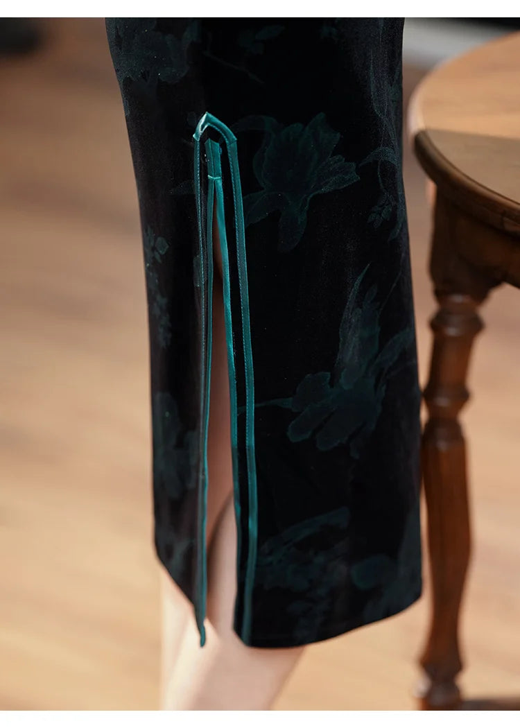 Black velvet pants with green floral embroidery on a wooden floor.
