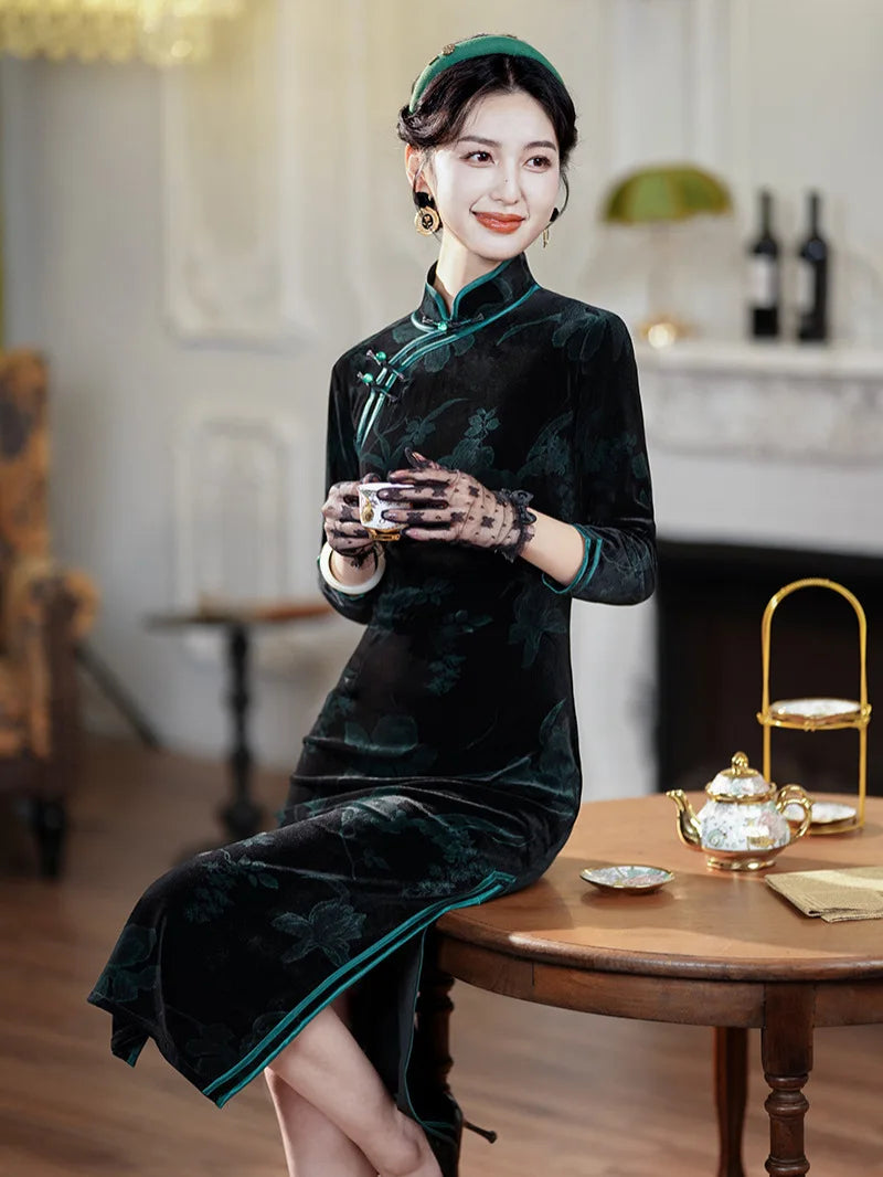Woman in a Black & dark Green Velvet Long Sleeves Qipao cheongsam Dress  sitting at a table with a teapot, holding a teacup.