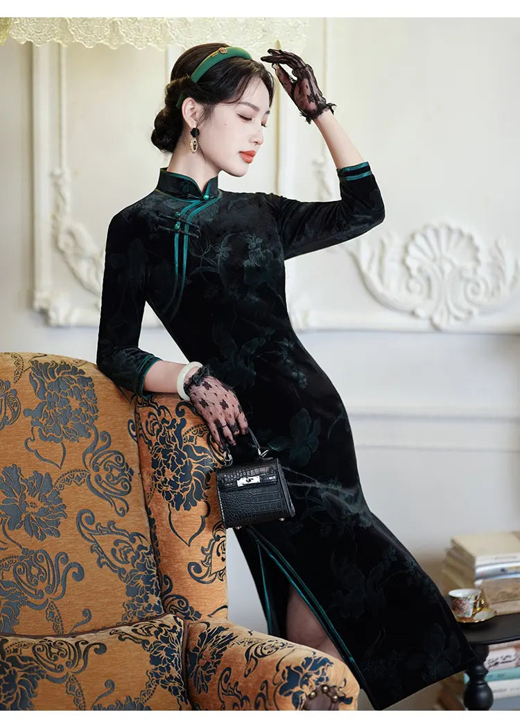 Woman in a Black & Emerald Green Velvet Long Sleeves Qipao Dress  sitting on an ornate chair in a decorated room.