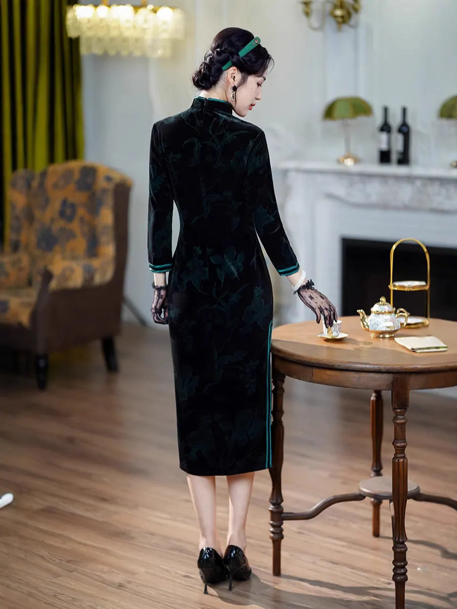 Woman in a Black & Emerald Green Velvet Long Sleeves Qipao Dress  standing in a room with a table and chairs.
