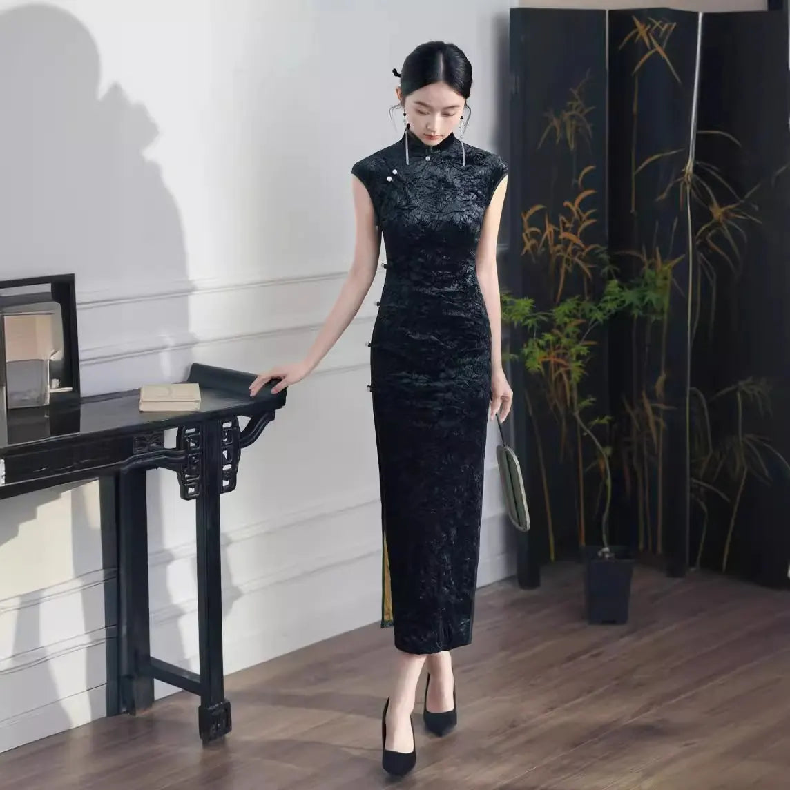 Woman in a Black Floral Velvet Qipao Cheongsam Dress  standing in a room with a decorative screen and plant.
