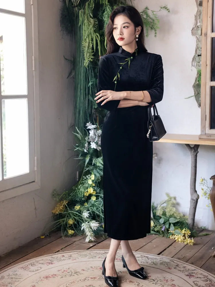 Woman in a Black Long Sleeves Qipao Dress with Green Embroidery  standing in a room with plants and a window.