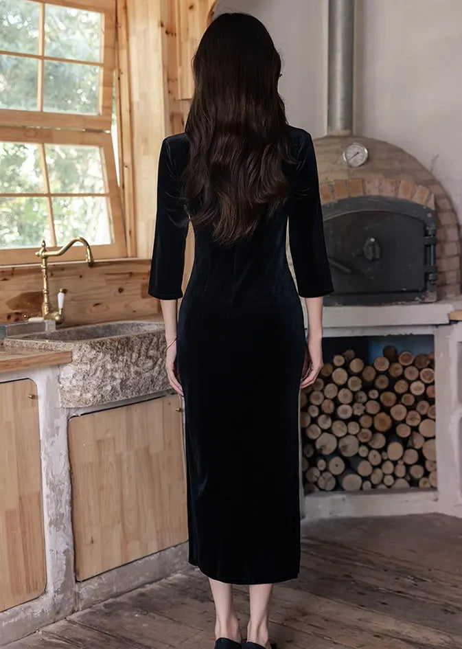 Woman in aBlack Long Sleeves Qipao Dress with Green Embroidery  standing in a rustic kitchen with wooden cabinets and a stone oven.