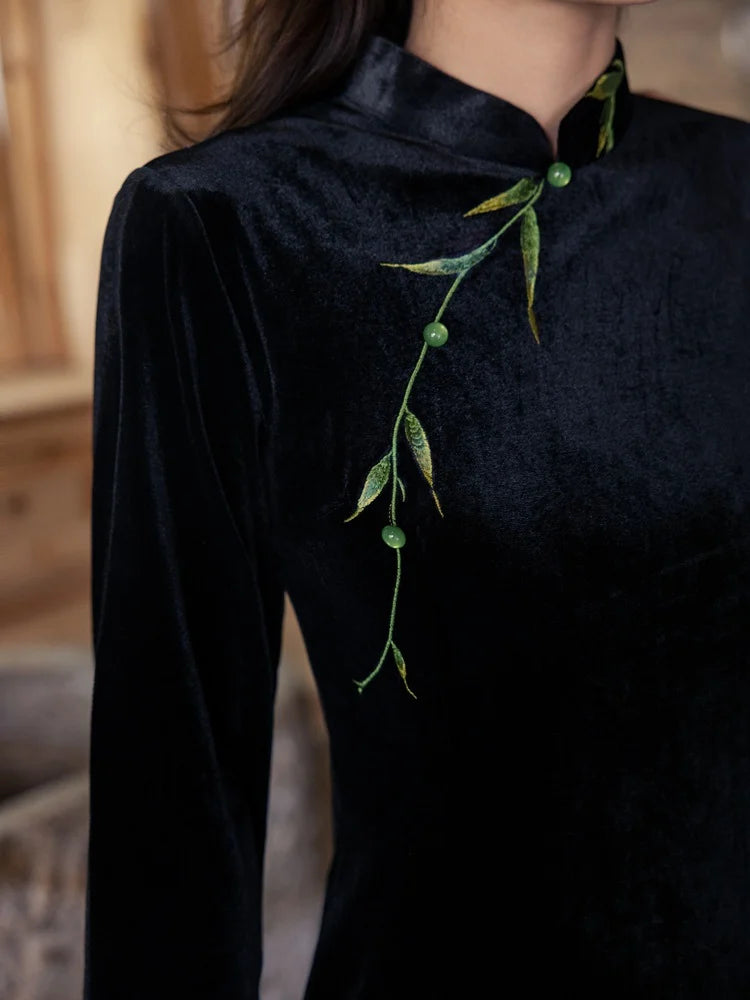 Black long-sleeve top with green leaf-like embellishments on a blurred background