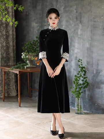 Woman wearing a Black Long Sleeves Velvet A-Line Qipao with Lace Trim  in a room with a gray wall and wooden table.
