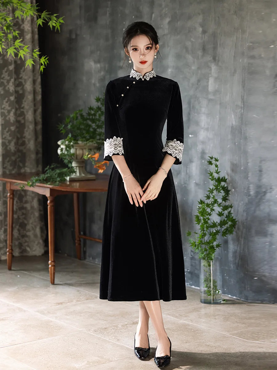 Woman wearing a Black Long Sleeves Velvet A-Line Qipao with Lace Trim  in a room with a gray wall and wooden table.