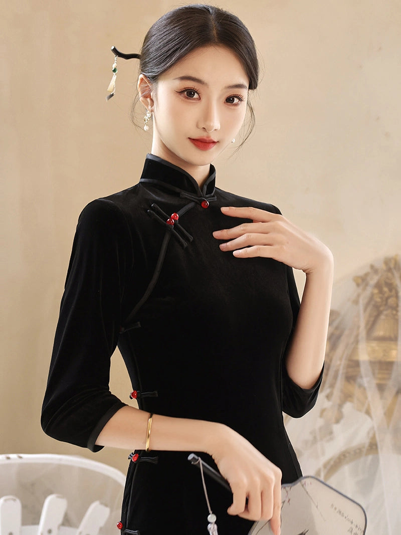 A woman wearing a black velvet Chinese cheongsam-style top with red button accents, posed against a warm beige background.