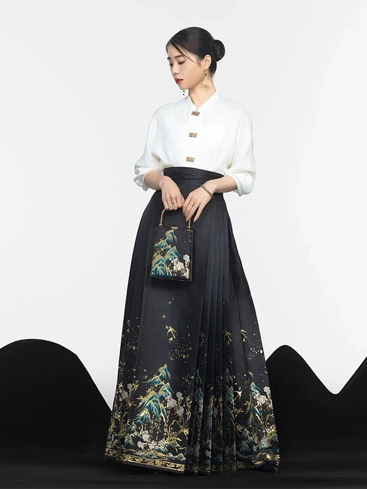 A woman models a traditional Chinese Hanfu outfit consisting of a white high-collar blouse and a long black pleated mamian horse face skirt with a detailed multicolor landscape print. She is holding a matching handbag against a clean white studio background.