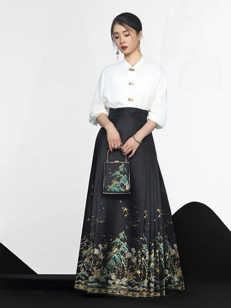 A woman models a high-waisted black mixi pleated mamian horse face skirt with a gold and green landscape print, paired with a white long-sleeve blouse, holding a small black handbag.