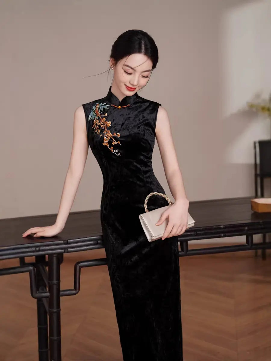 Woman in a Black Modern Velvet Sleeveless Embroidered Qipao  dress with floral embroidery holding a clutch in an indoor setting