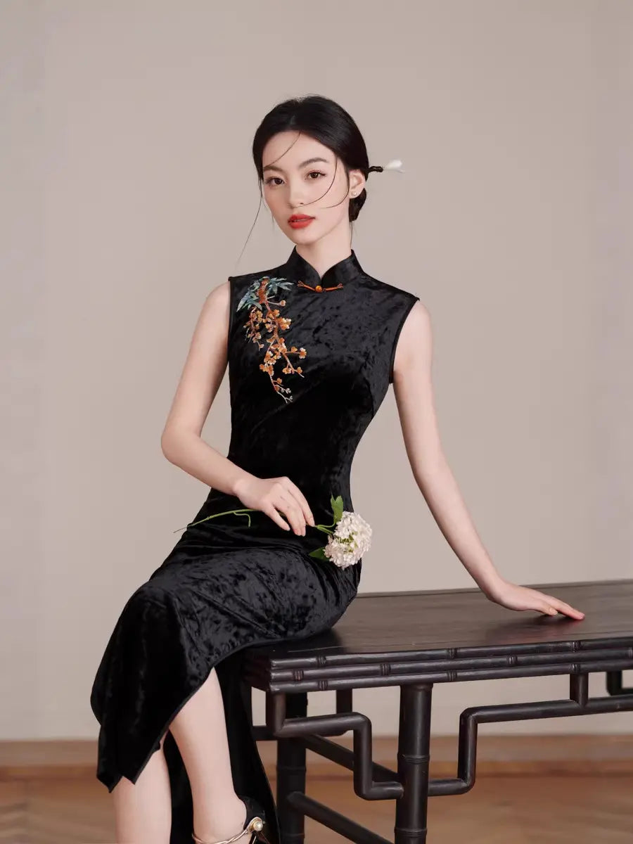 Woman in a Black Modern Velvet Sleeveless Embroidered Qipao  dress sitting on a wooden table against a plain background