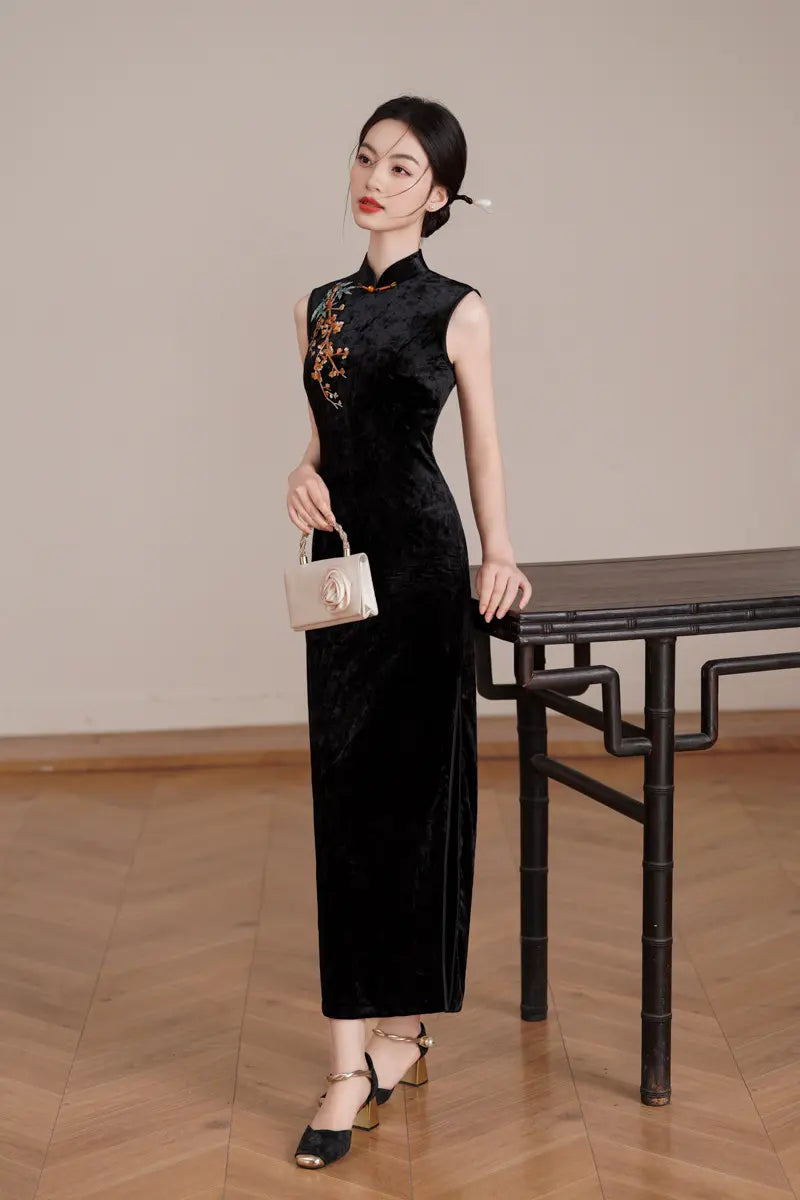 Woman in a Black Modern Velvet Sleeveless Embroidered Qipao  dress with floral embroidery standing in a room with wooden floor and table.