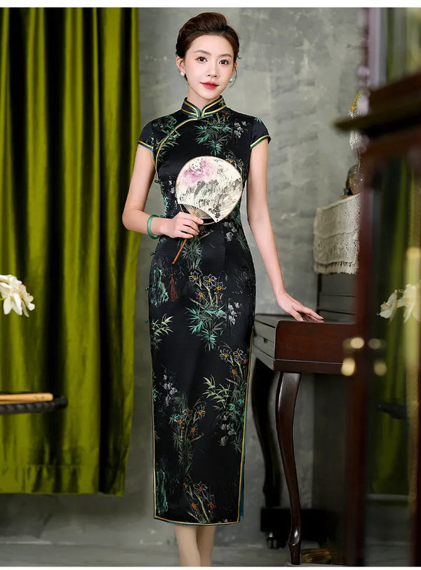 Woman in a traditional floral Black Silk Qipao Dress with Bamboo & Orchid Print holding a fan in an indoor setting.