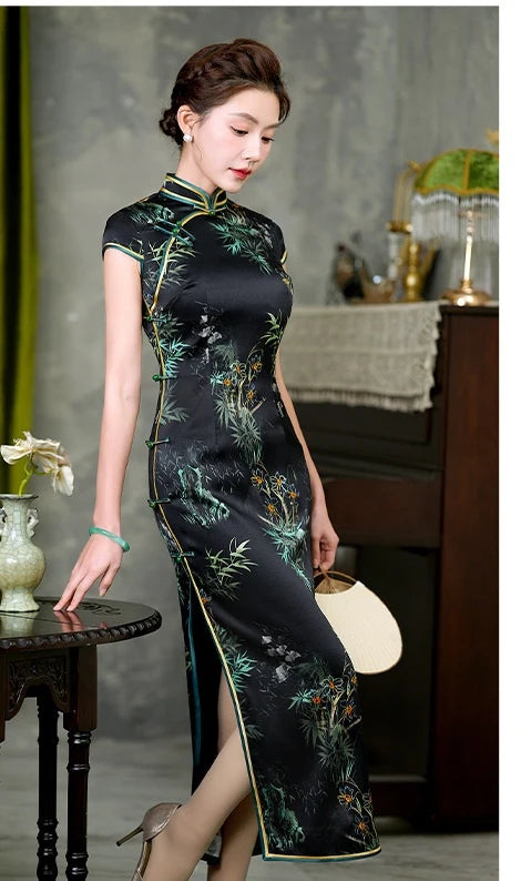 Woman wearing a traditional Black Silk Qipao with Bamboo & Orchid Print dress with green floral patterns in an indoor setting.
