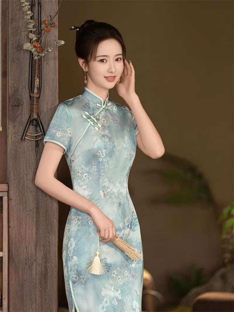 Woman in a light blue floral cheongsam standing against a wooden door.