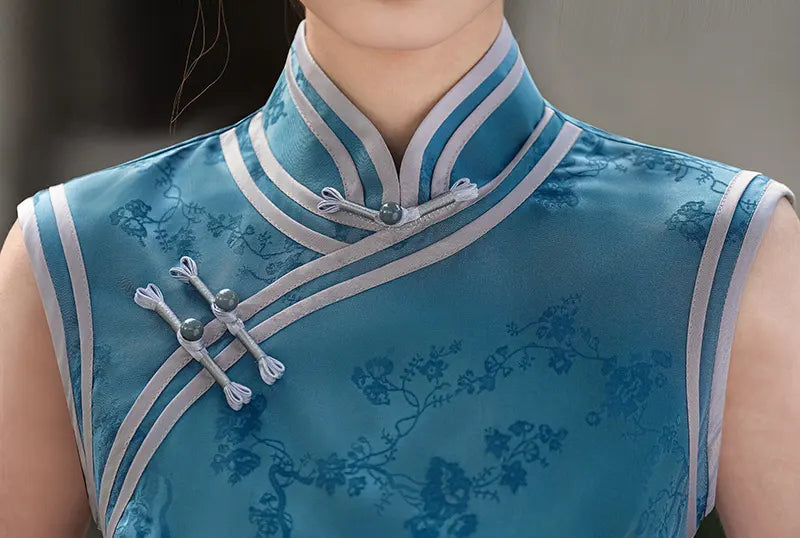 Blue traditional qipao dress with floral patterns and white accents on a neutral background