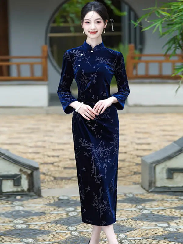 A woman stands outdoors in a traditional courtyard wearing a dark navy Velvet Long Sleeve Qipao cheongsam-style dress with light floral embroidery. The dress has three-quarter sleeves, a mandarin collar, and a fitted silhouette.