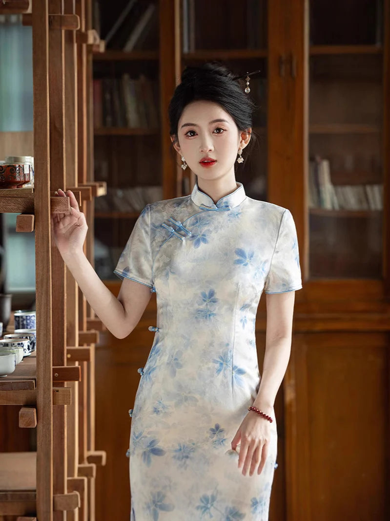 Woman in a Blue Watercolor Floral Long Qipao Cheongsam Dress  standing in a room with wooden furniture and books.