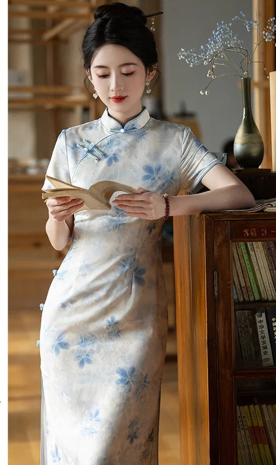 Woman in a Blue Watercolor Floral Long Qipao Cheongsam Dress reading a book in a room with wooden furniture and books.