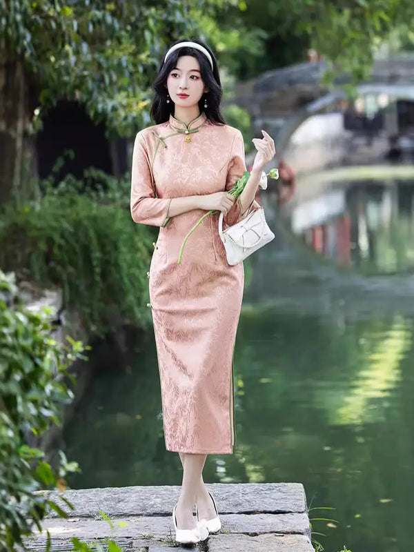 Woman in aBlush Pink Long Sleeves Qipao Cheongsam Dress with Bamboo Pattern standing by a body of water with greenery.