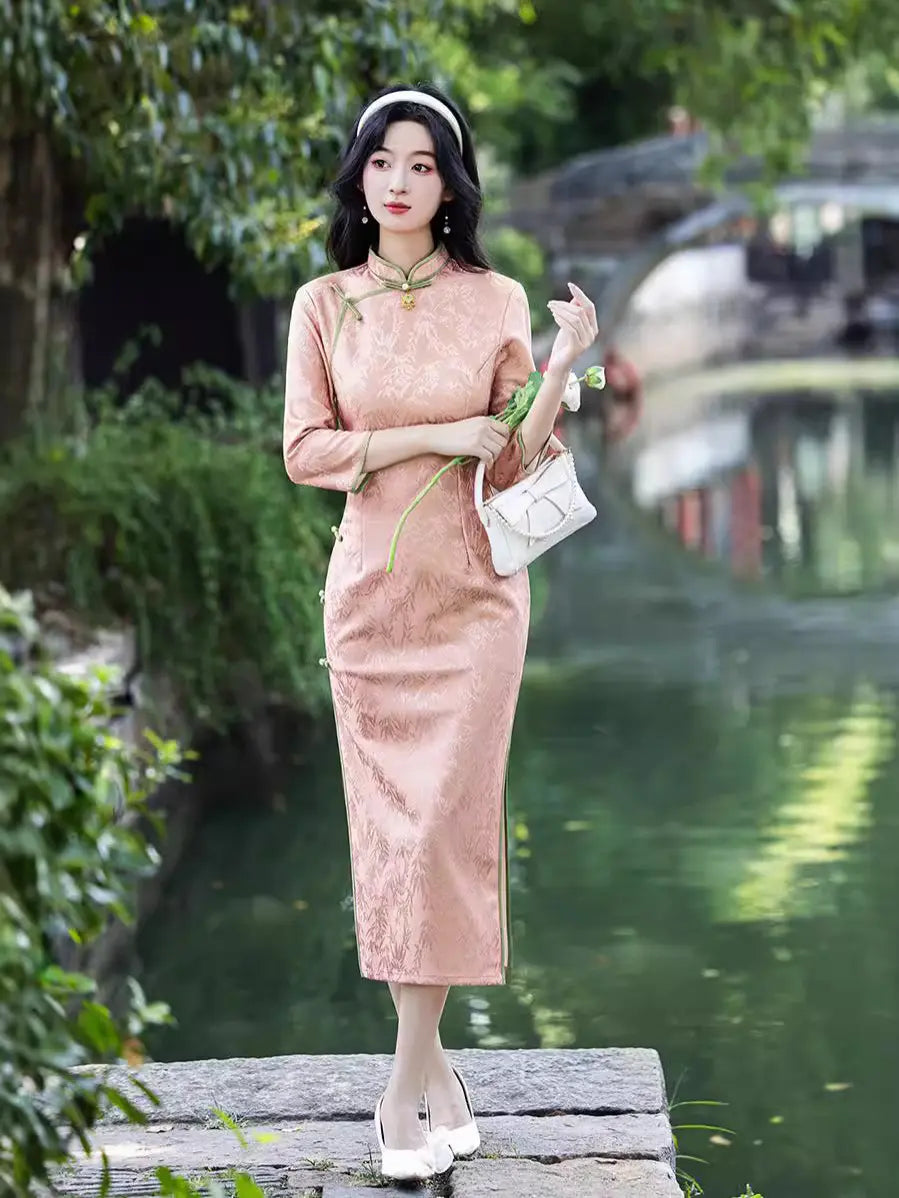 Woman in aBlush Pink Long Sleeves Qipao Cheongsam Dress with Bamboo Pattern standing by a body of water with greenery.
