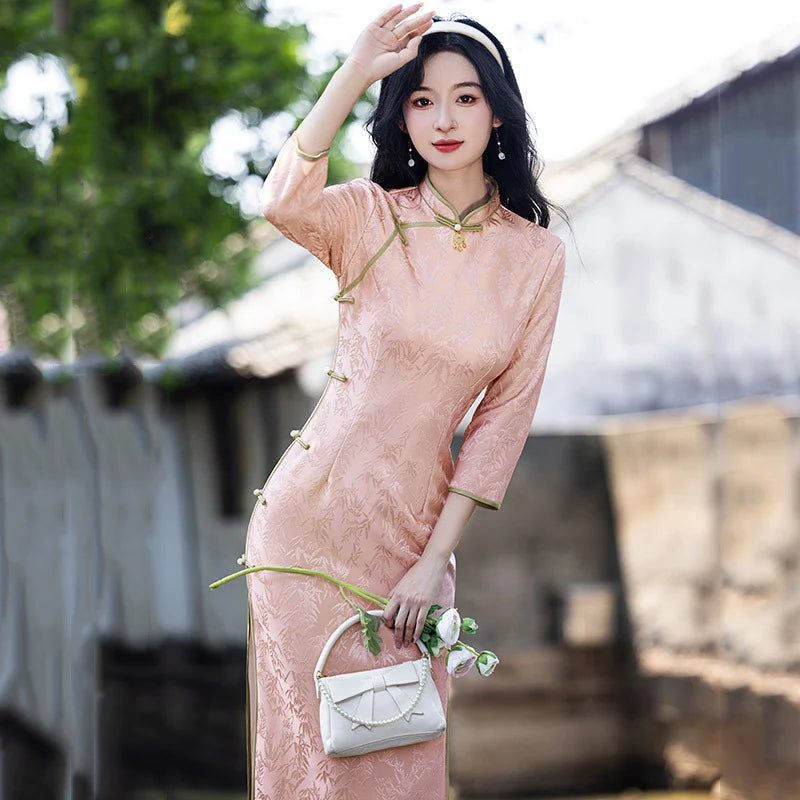Woman in a traditional Blush Pink Long Sleeves Qipao Cheongsam Dress with Bamboo Pattern holding a white handbag outdoors.