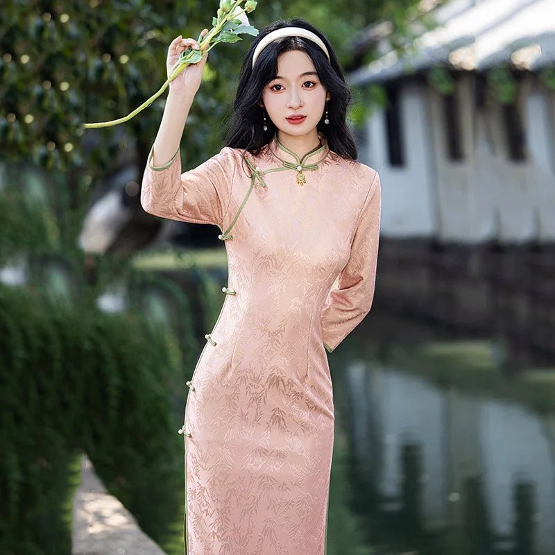 Woman in a traditional Blush Pink Long Sleeves Qipao Cheongsam Dress with Bamboo Pattern holding green leaves in a garden setting