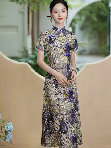 A woman wearing a short-sleeved Botanical Violet & Olive Floral Jacquard Modern A Line Qipao cheongsam dress in purple, gold, and beige tones, standing in front of a beige decorative wall with a blurred outdoor background.