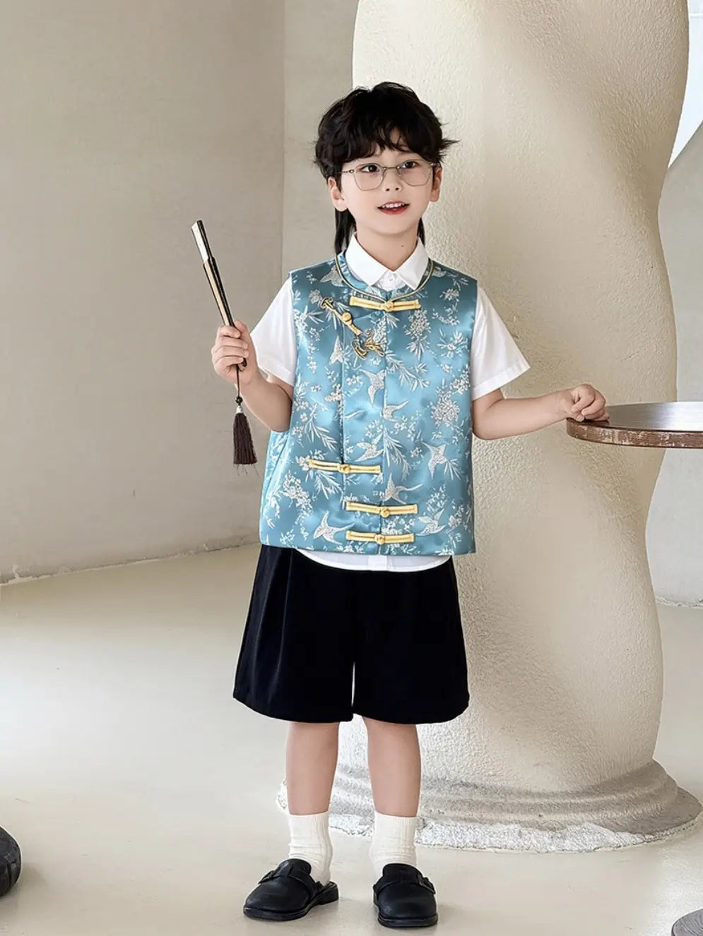 Child wearing a Elon's son outfit Traditional Chinese Style Blue Vest & Shorts Outfit over a white shirt and black shorts, holding a broom.