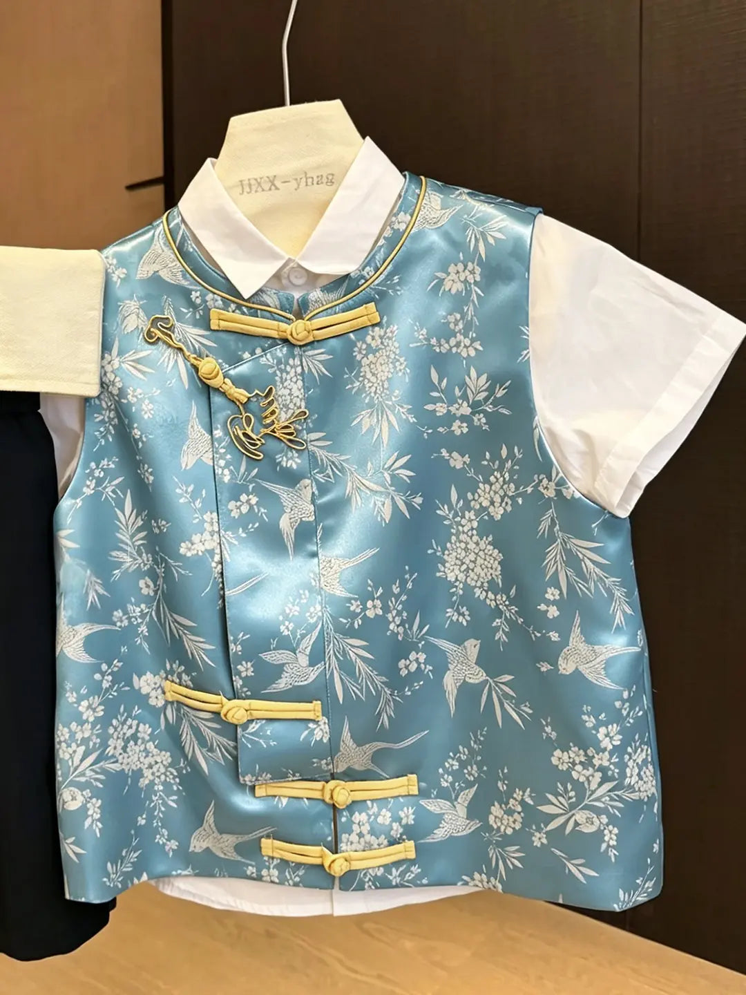 Traditional Chinese outfit with floral pattern on a hanger against a dark background