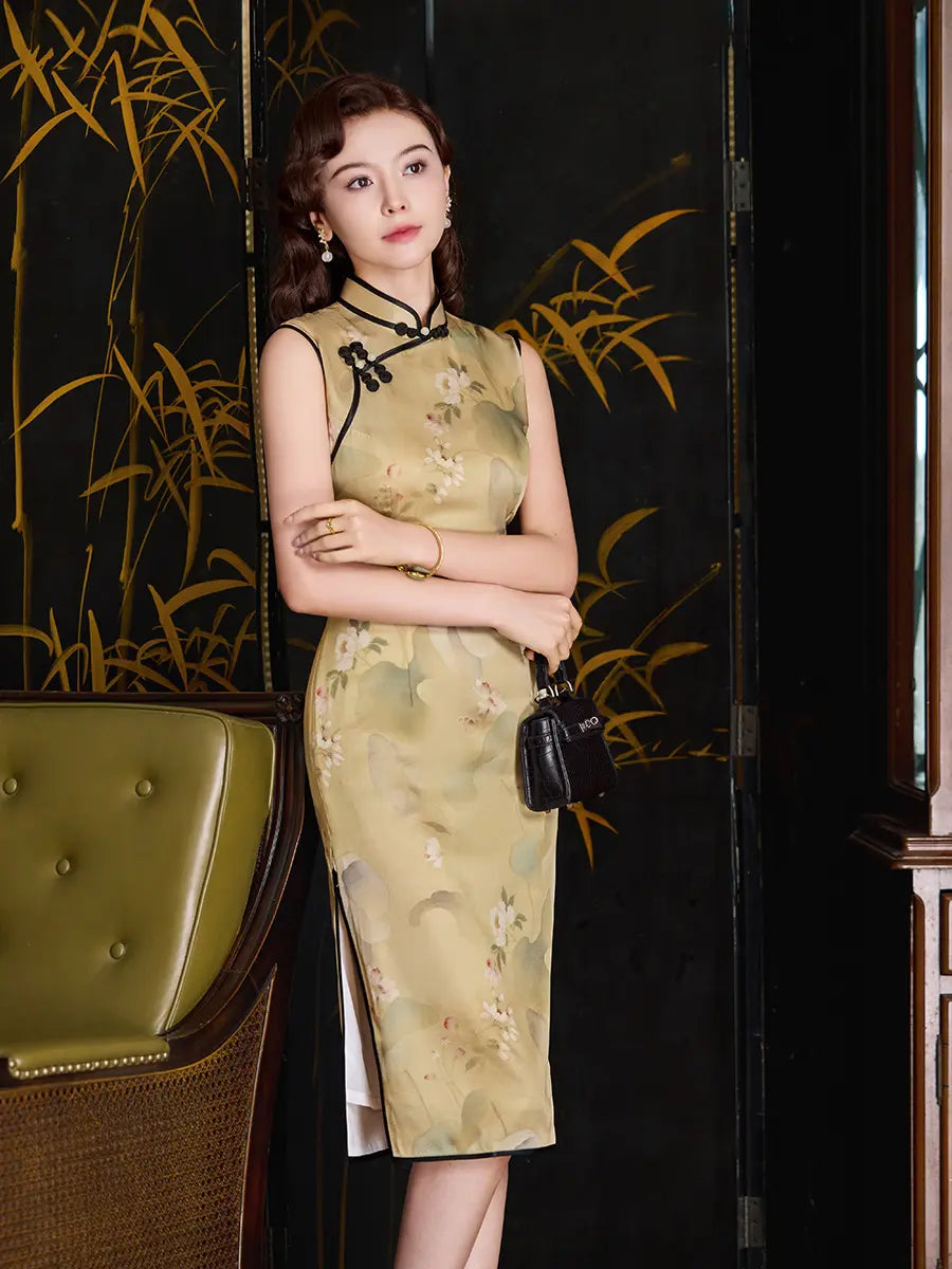 A woman models a sleeveless beige silk cheongsam dress with a subtle floral print, black collar trim, and black tie details. She is standing in front of a black folding screen with gold bamboo designs, holding a small black handbag.