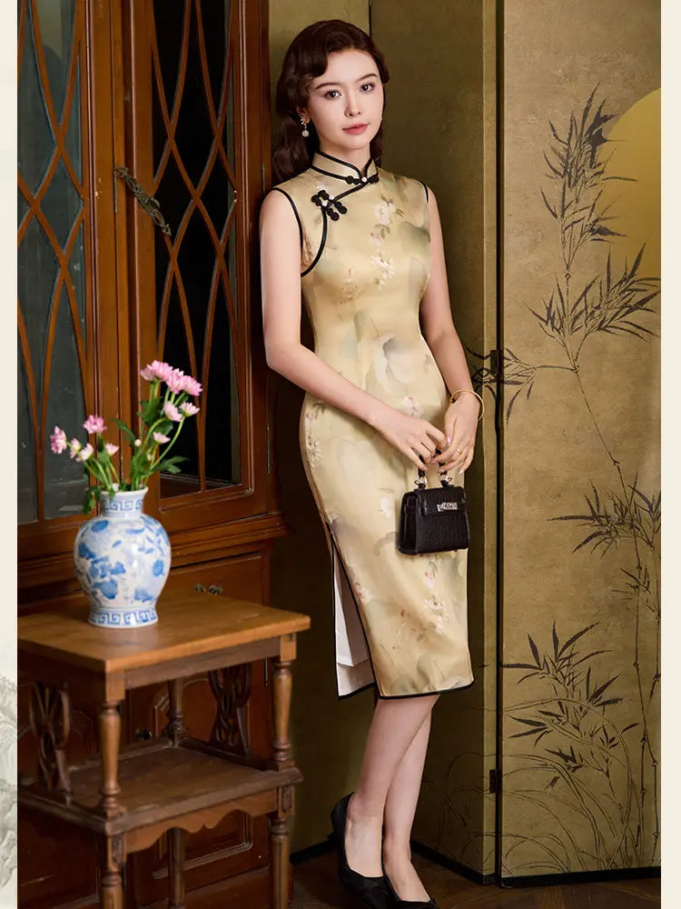 A woman models a sleeveless beige and gold floral-patterned silk qipao cheongsam dress with black trim, standing in a traditional room next to a wooden cabinet and folding screen.