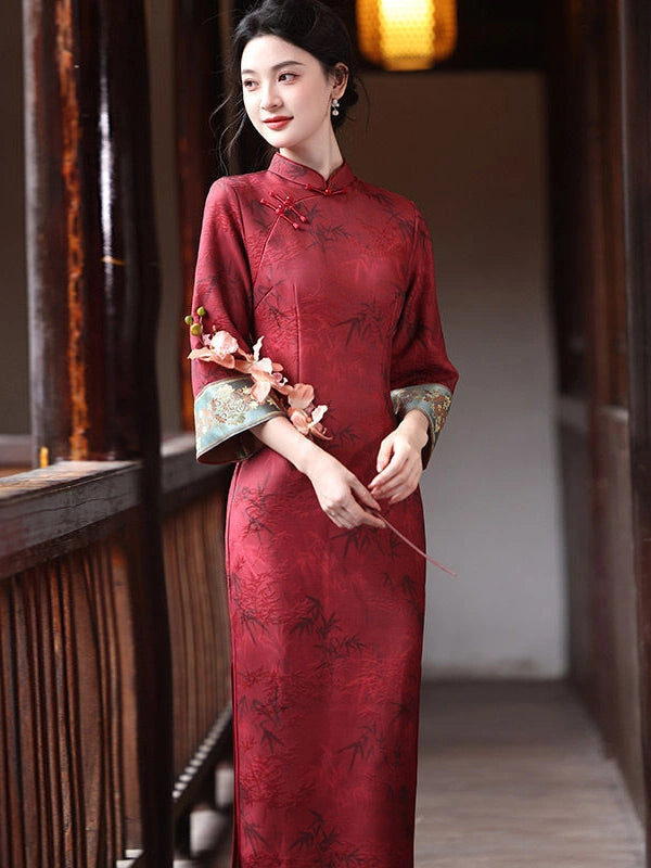 A woman wearing a traditional Chinese Crimson Red Bamboo Jacquard Long Sleeve Qipao With Embroidered Cuff , standing in a wooden corridor holding a small bouquet of pink flowers.