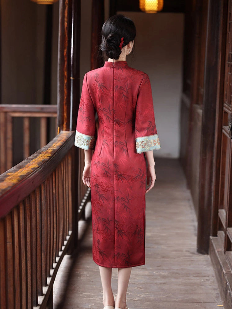 A woman viewed from behind wearing a red Chinese cheongsam dress with a subtle floral pattern and light blue patterned cuff trim, standing on a wooden corridor.
