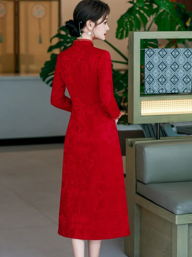 A woman wearing a long-sleeved red textured a line  cheongsam-style dress, photographed from behind in an indoor setting with plants and furniture visible.