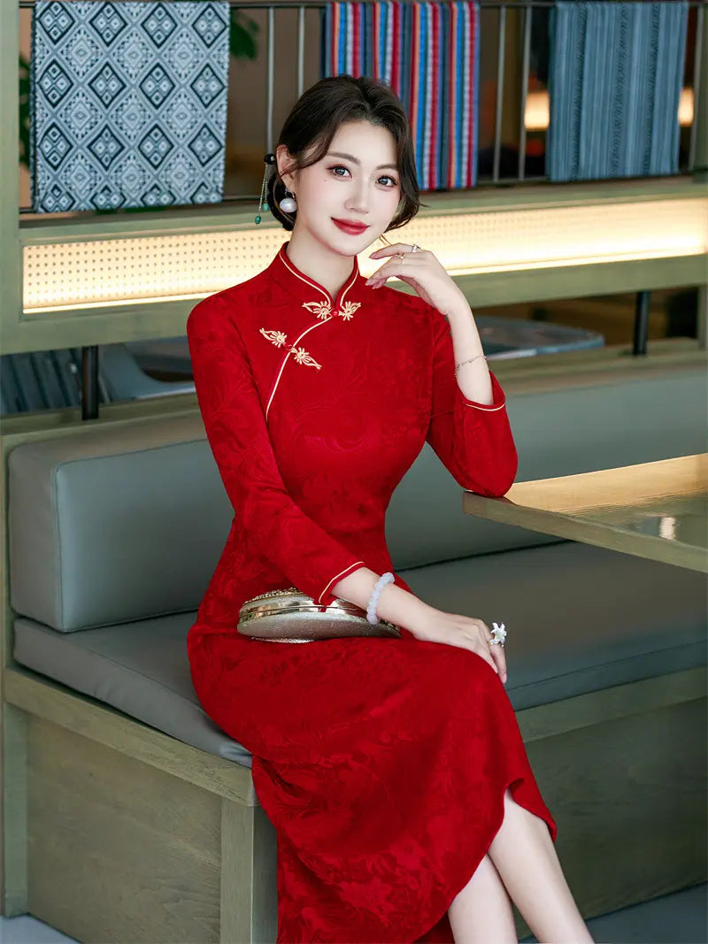 A woman wearing a red long-sleeve a line cheongsam dress with gold embroidery sits on a modern cafe bench, holding a metallic clutch.