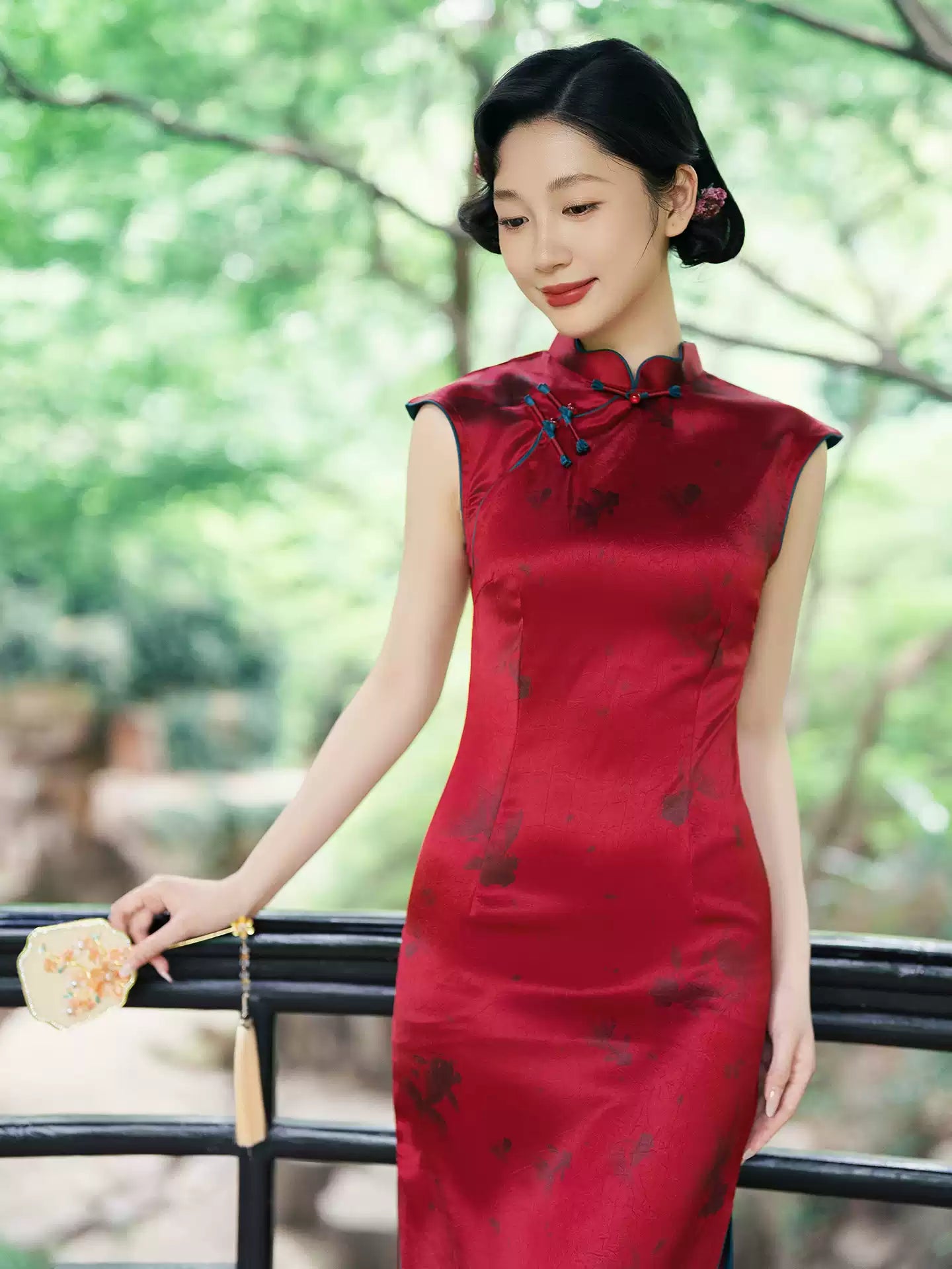 Woman in a traditional Crimson Red Sleeveless Goldfish Qipao  dress standing outdoors with greenery in the background