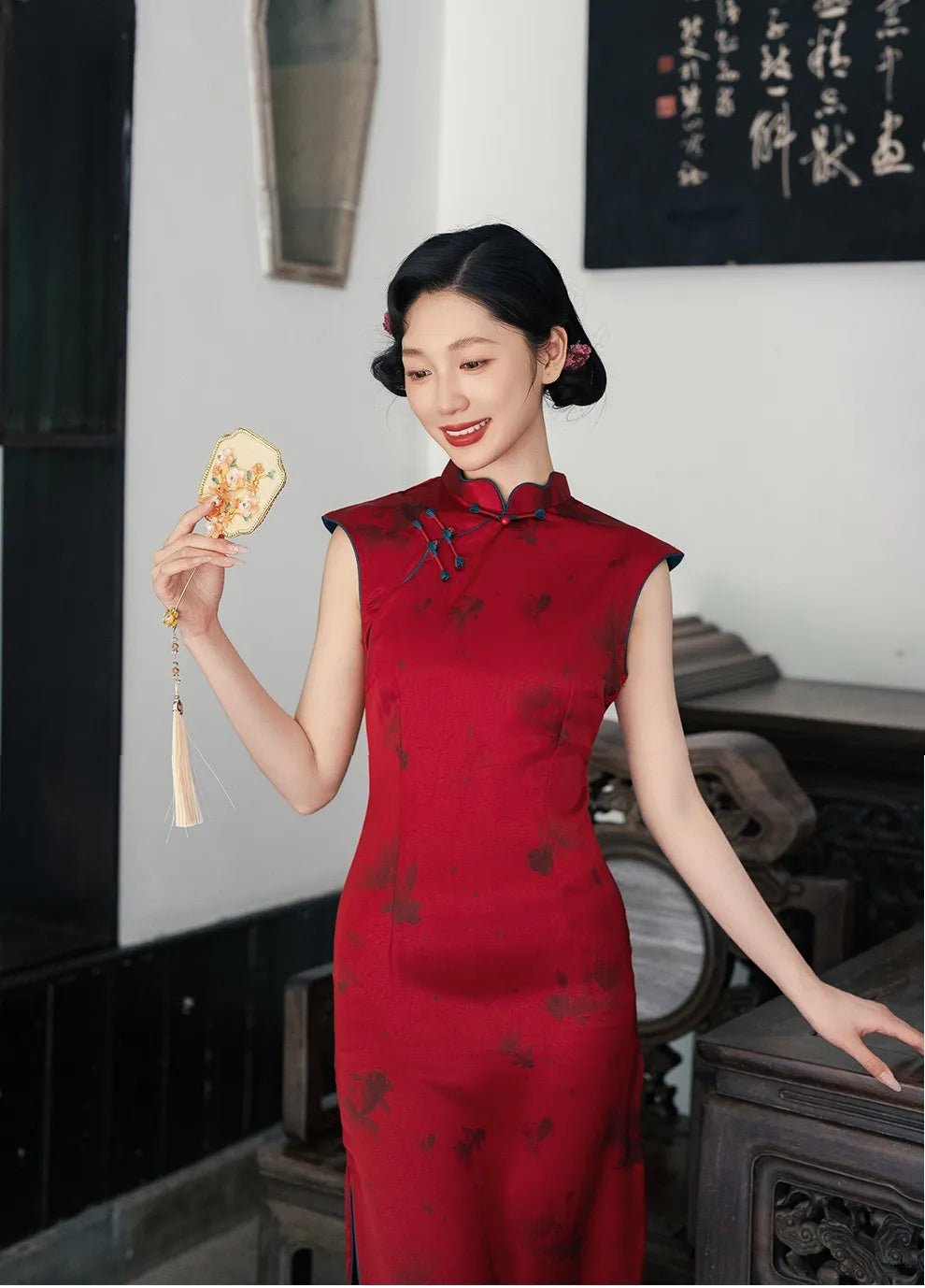 Woman in a Crimson Red Sleeveless Goldfish Qipao Dress  holding a decorative item in an indoor setting.