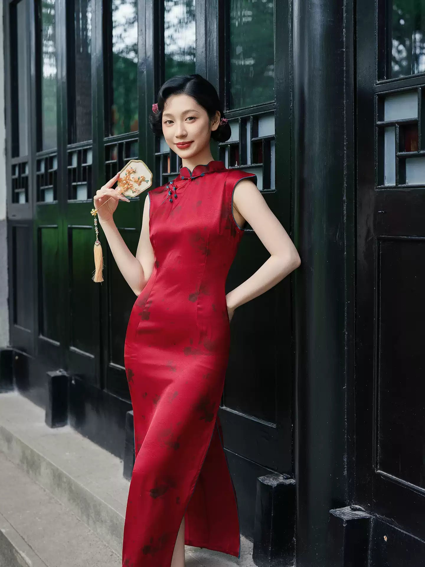 Woman in a Crimson Red Sleeveless Goldfish Qipao Dress  standing against a black wall.