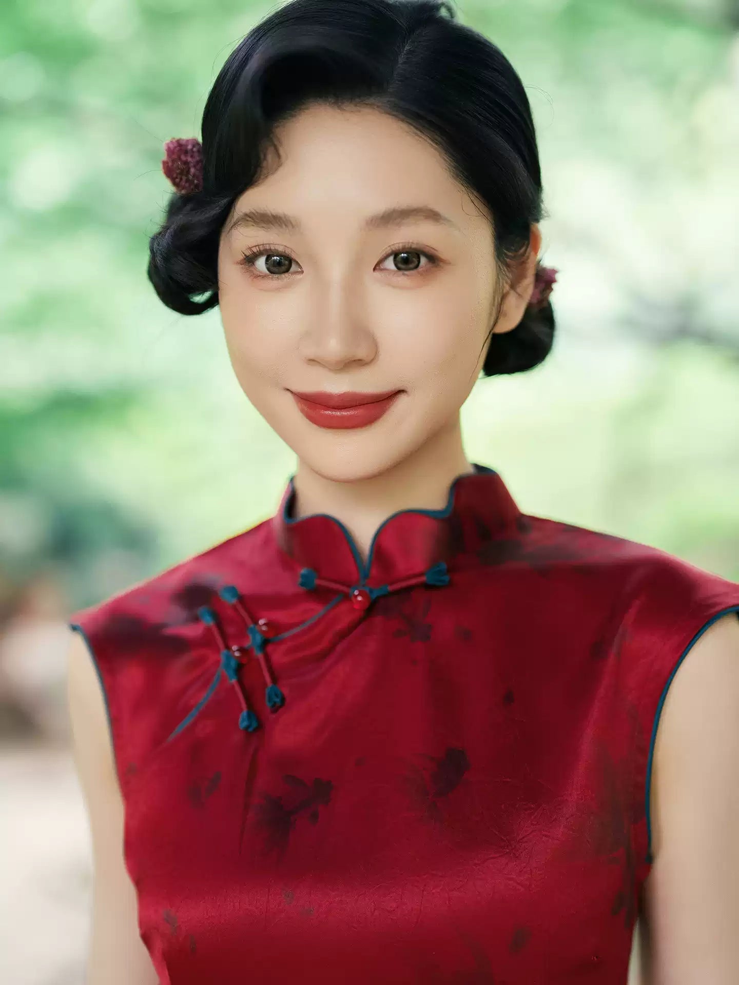 Woman wearing a traditional Crimson Red Sleeveless Goldfish Qipao Dress  with a blurred green background