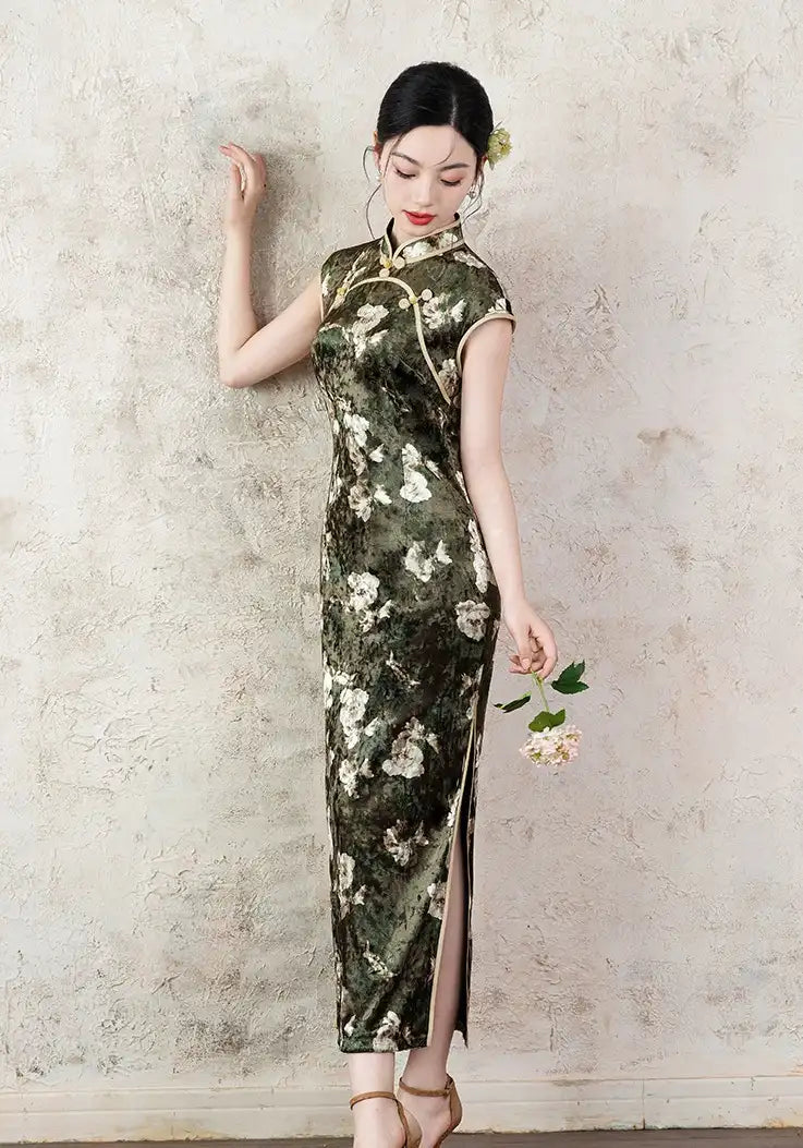 Woman in a Dark Green Foral Velvet Cap Sleeves Long Qipao Dress  holding a flower against a textured wall.
