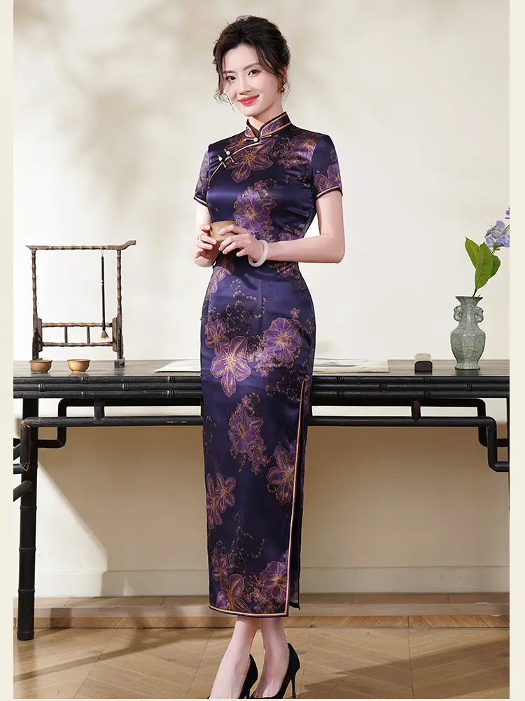 Woman in a Deep Amethyst Purple & Gold Floral Silk Long Chinese Qipao  dress standing in a room with a table and decorative items.