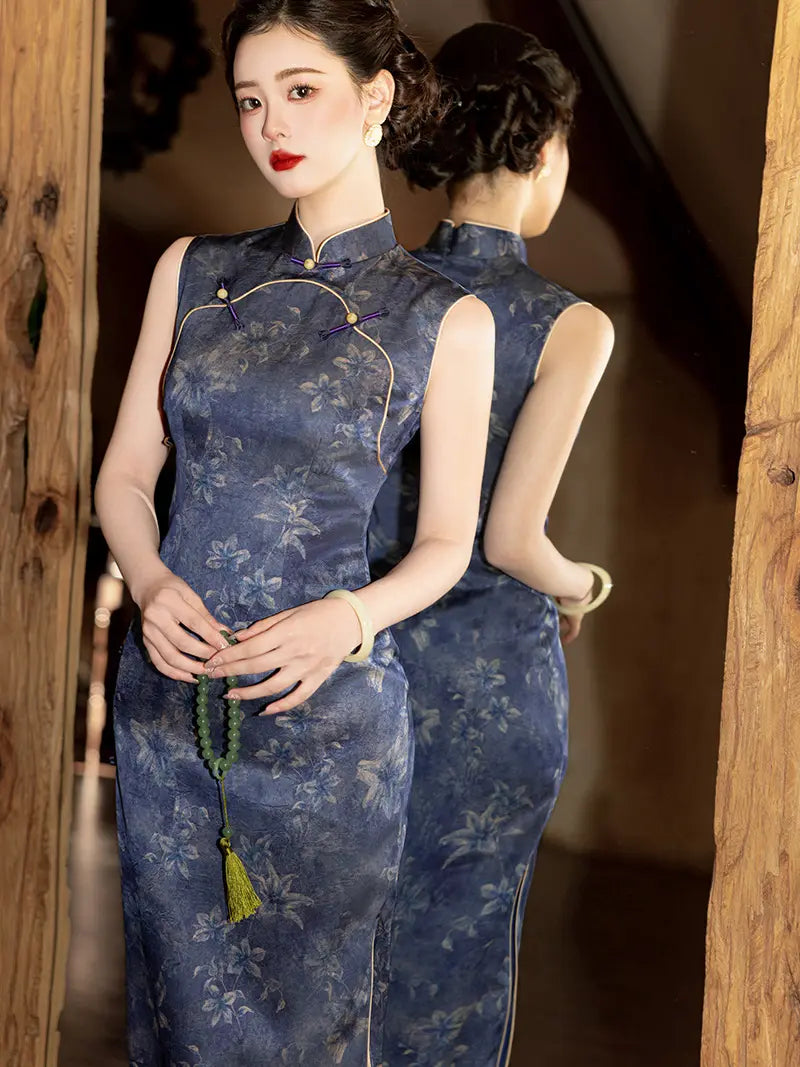 A woman wearing a sleeveless blue floral cheongsam with gold trim, standing in a doorway with a mirror behind her showing the back view of the dress.