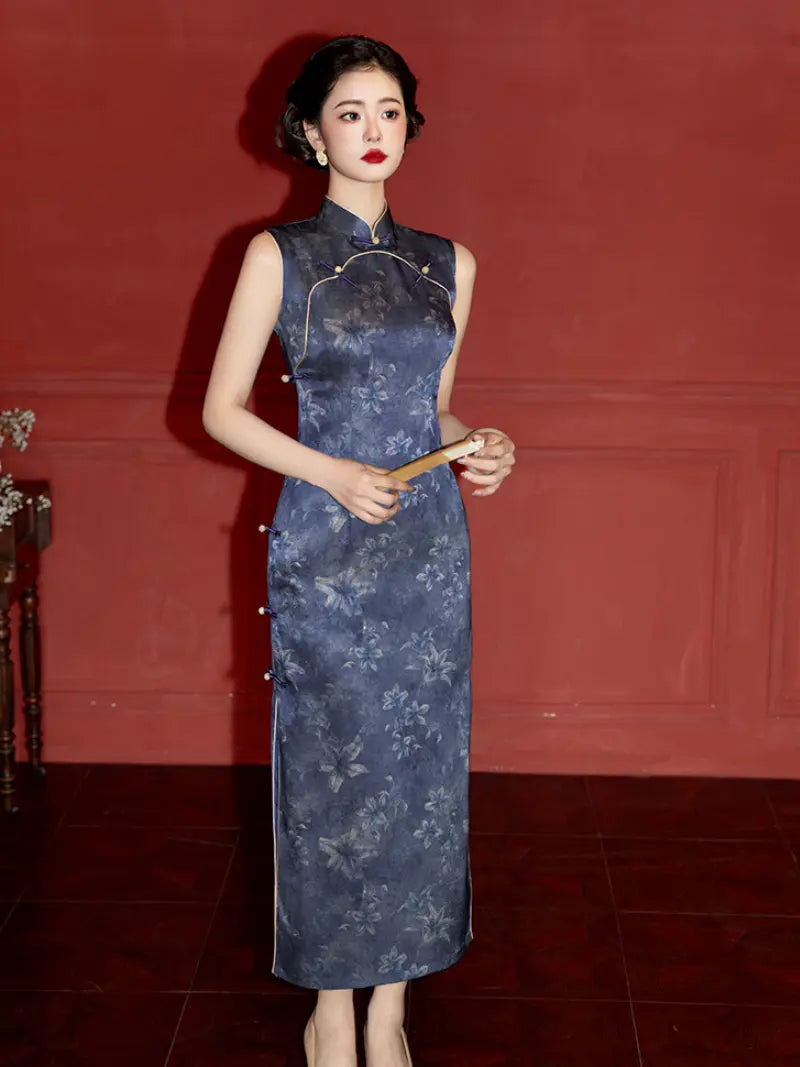 A woman wearing a sleeveless dark blue floral-patterned cheongsam dress, holding a small fan against a dark red paneled wall background.