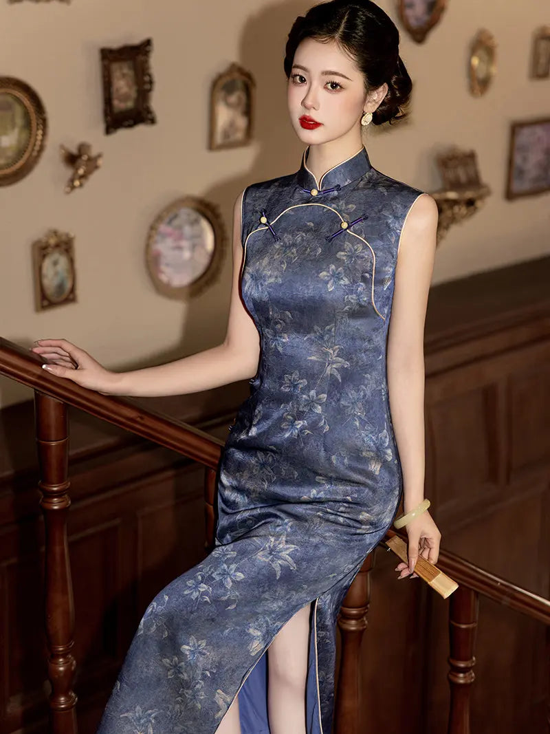 A woman wearing a sleeveless blue floral-patterned cheongsam dress with gold trim, posing on a wooden staircase in an elegant interior setting.