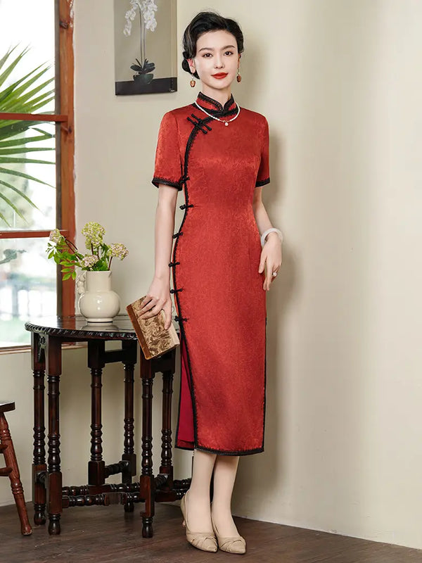 Full-length shot of a woman in a deep crimson silk jacquard qipao with black lace trim and frog buttons, standing in a vintage-style room