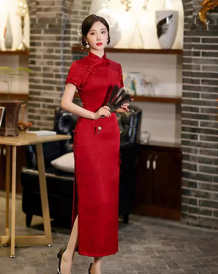 Woman in a Deep Red Floral Long Qipao Cheongsam Dress with Lace Trim holding fans indoors with decorative elements.