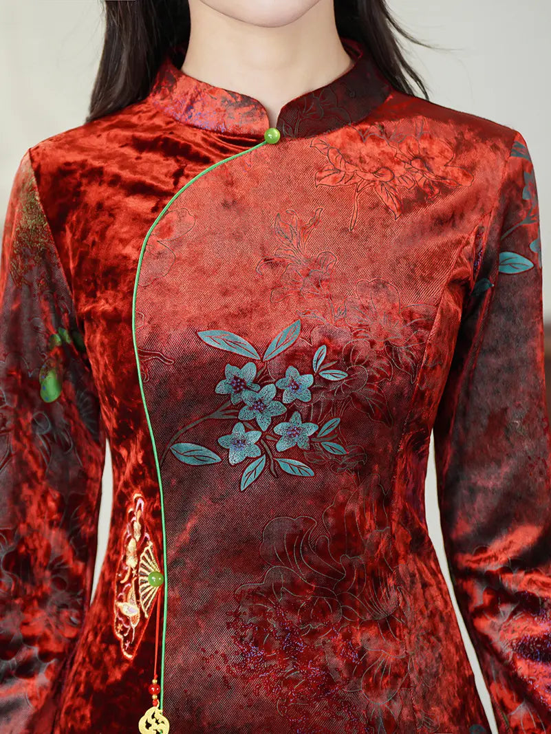 A close-up of a red velvet cheongsam-style dress with floral print , featuring a mandarin collar, green button, and a green cord with a gold tassel.